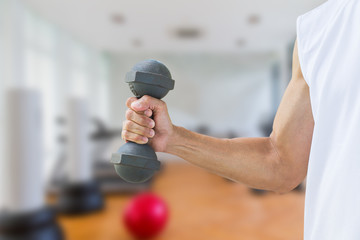 Man wearing sleeveless white shirt holding old dumbbell on blurred gym background
