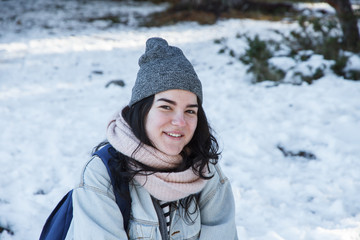 Fototapeta na wymiar Young caucasian white woman with brown eyes wearing a cap and warm clothes in the snow. She enjoys a winter vacation trip in the snowy forest. 