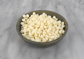 White chocolate baking chips in a bowl atop a gray marble cutting board.