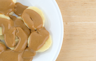 Ripe cut bananas covered with peanut butter on plate atop a wood table.