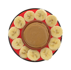 Ripe banana slices in a circle around peanut butter isolated on a white background.