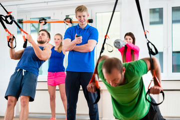 Sportler und Sportlerinnen beim Ringeturnen im Fitness-Club mit Physiotherapeut