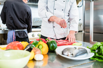 Obraz na płótnie Canvas Chef putting salt on fish while cooking in kitchen
