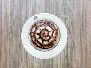 Top view of latte coffee with art on white cup and dish,  wooden table