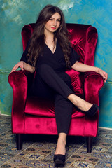 beautiful girl in a black trouser suit sitting on a red chair