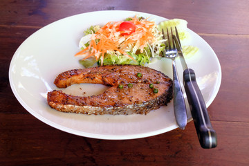 salmon steak grilled with black pepper on white dish with fork a