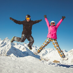 Happy couple of snowboarders jumping in the alpine mountains