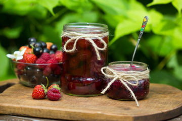strawberry, blackcurrant and raspberry. Berry jam in a jar on wooden background.