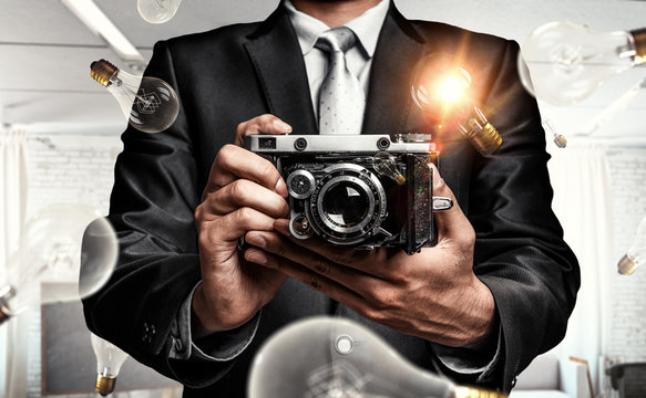 Businessman taking photo with vintage camera . Mixed media