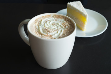 Mocha with whipped cream in coffee mug and coconut cake on black table background