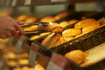 hand with tongs taking bun at bakery or grocery