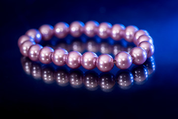 bracelet of pink yellow pearls with reflection isolated on dark blue.
