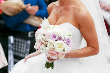 Bride with bronze skin holds white bouquet of roses and peonies