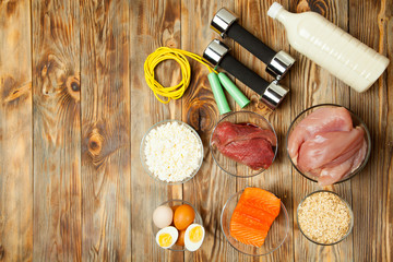 Fototapeta na wymiar Protein, fish, cheese, eggs, meat, chicken and dumbbells on a wooden background