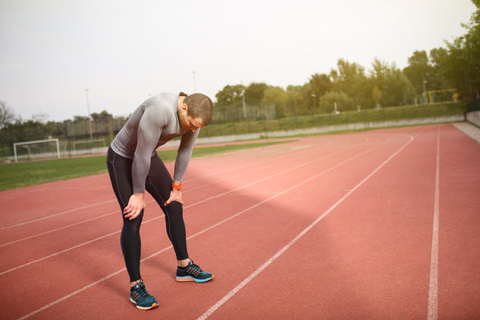 Young athletic tired sprinter having a break. Standing on a track catching his breath.