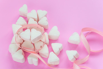 Fototapeta na wymiar Marshmallows in heart shapes for Valentines day over pink paper background and ribbon to celebrate sweet love candy for couples, selective focus