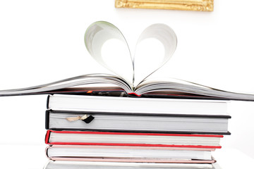 Auf einem Stapel Bücher ist das obere aufgeschlagen und die Seiten bilden ein Herz