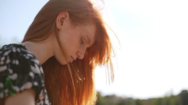 Dreamy redhead girl sitting watching touching hair while wind genlty blowing in slowmotion. Close up