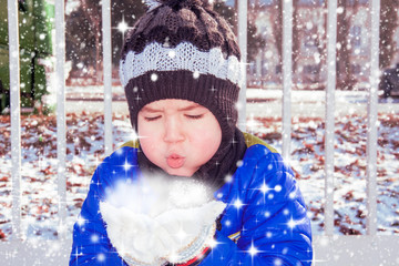 Portrait of cute little boy blowing magic snow from his hands on a winter day