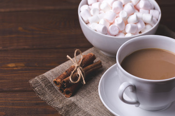 Fototapeta na wymiar Cup of hot coffee or cocoa, cinnamon and plate with marshmallows on wooden table