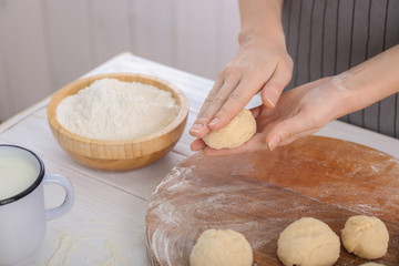 Woman making buns from raw dough on kitchen table