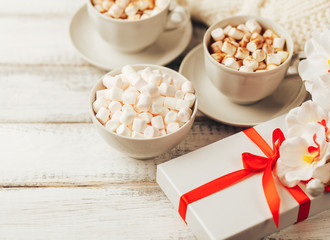 Cups with hot coffee or cocoa and marshmallows, gift box with red ribbon