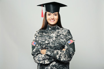 Pretty female soldier wearing graduation cap, on grey background