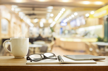 Cup of coffee and tablet on wooden table in coffee shop.