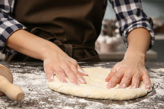Young woman making dough in kitchen, closeup