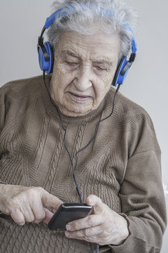 Senior woman listening music with headphones and smart phone
