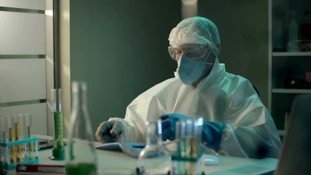 Crazy mad scientist in respirator drinks poisonous toxic liquid substance after performing an experiment in modern chemical laboratory. Unsuccessful test of new green beverage. Joke in chemical lab