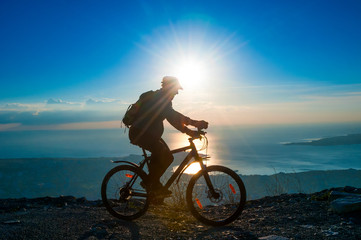 Fototapeta na wymiar Silhouette of senior cyclist rides on a bike in mountain at suns