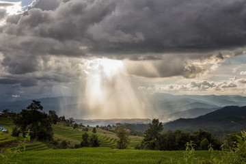 Storm clouds with rain and sunbeam over the mountain