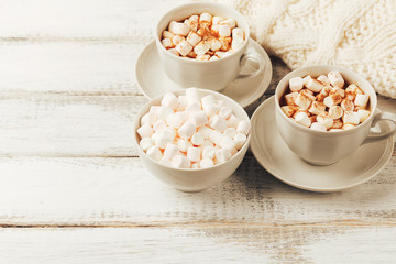 Cups with hot coffee or cocoa and marshmallows, white knitted blanked 