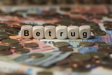 betrug - Holzwürfel mit Buchstaben im Hintergrund mit Geld, Geldscheine