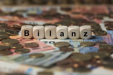 bilanz - Holzwürfel mit Buchstaben im Hintergrund mit Geld, Geldscheine
