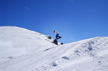 Snowboarder jumping in terrain park at ski resort on sun winter