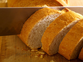 slicing baguette on a cutting board with chef's knife, shallow depth of field, selective focus, macro