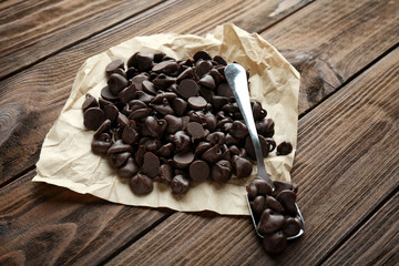 Tasty chocolate chips, parchment and spoon on wooden background