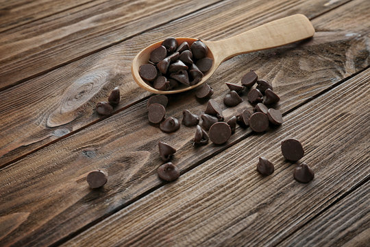 Tasty chocolate chips and spoon on wooden background