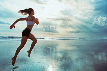 Active sporty woman run along ocean surf by water pool to keep fit and health. Sunset black sand beach background with sun. Woman fitness, jogging workout and sport activity on summer family holiday. - Powered by Adobe