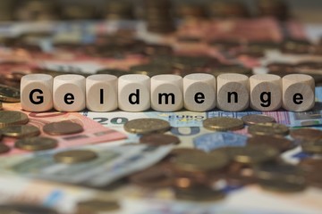 geldmenge - Holzwürfel mit Buchstaben im Hintergrund mit Geld, Geldscheine