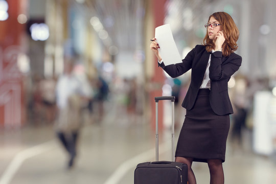 Business woman speaks on a mobile phone standing with the Luggage in the airport lounge.