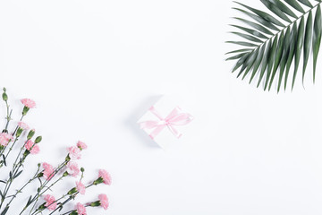 Small box with pink ribbon and flowers lie on a white table