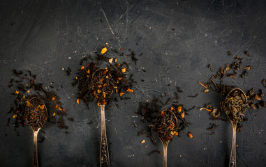 Selection of fragrant teas with dried fruits and spices in teaspoons, that a dark background, top view, copy space