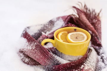 Obraz na płótnie Canvas mug of tea with lemon slice wrapped in a knitted scarf on the snow