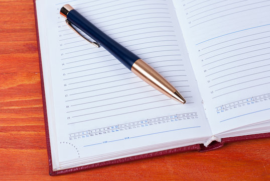 Business accessories - diary with a pen lying on a wooden table