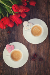 Two cups of Valentines day coffee with fresh tulips on wooden table, top view, retro toned