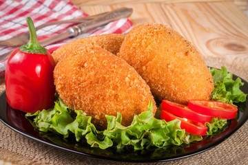 three fried breaded cutlet with lettuce on a black plate and wooden background