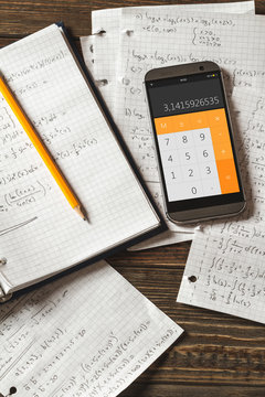 Solving mathematical problems in a notebook .  Phone with calculator app on wooden desk.